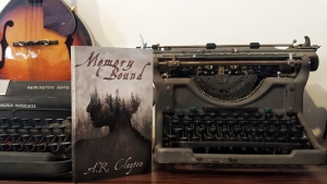 Memory Bound by A.R. Clayton between two vintage typewriters and a mandolin hanging on the wall behind them.