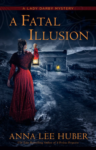 A Fatal Illusion by Anna Lee Huber cover. A woman with her back to the viewer stands on a path toward a cottage on the countryside. She is wearing a red dress with a darker shawl and holds a lantern up to a cottage at the end of the path.